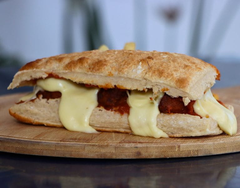 Sándwich de albóndigas con queso fundido sobre tabla de madera