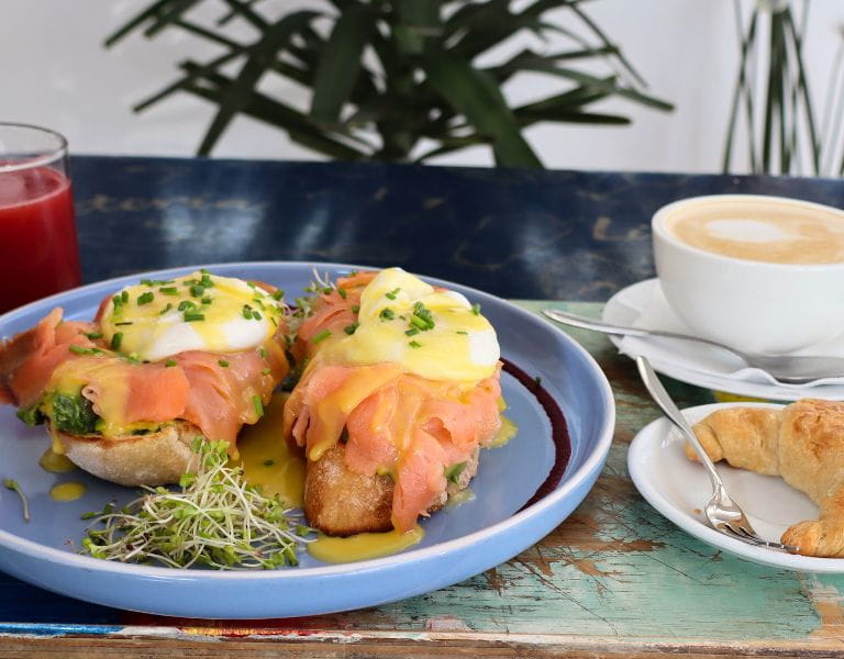 Tostadas benedictinas con salmón ahumado y salsa holandesa, junto a un café